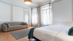 Ein Schlafzimmer mit einem Bett, einer Schlafcouch und einem großen Fenster mit Vorhängen.