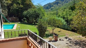 Un balcone con vista su un prato verde, una piscina e un pendio boscoso.
