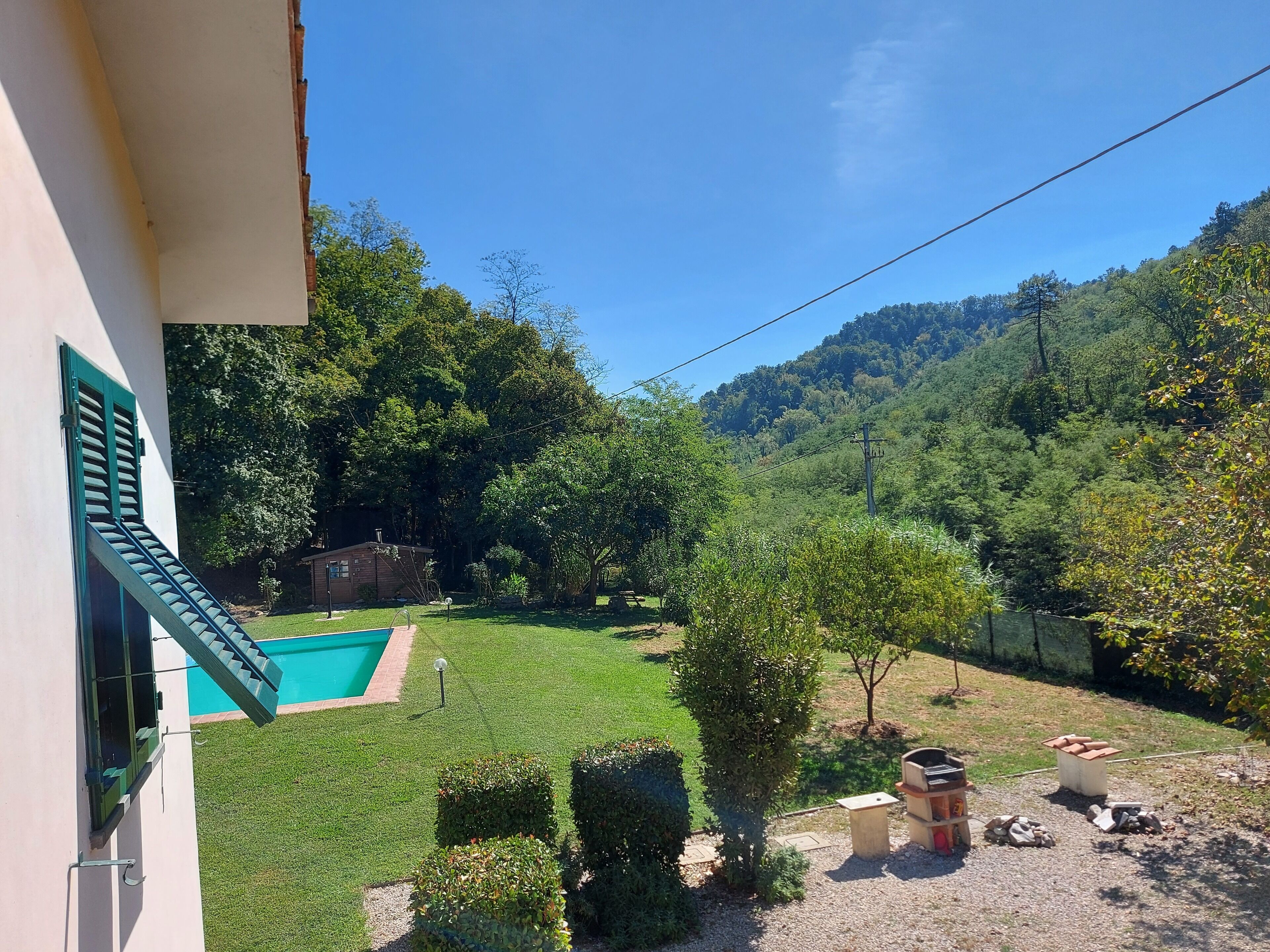 A residential property with a swimming pool, well-maintained lawn, and a view of a forested hillside.
