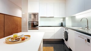 Une cuisine moderne avec des meubles blancs, un four à micro-ondes en acier inoxydable, un four encastré, un lave-linge et un plateau de petit-déjeuner avec de la nourriture et des boissons.