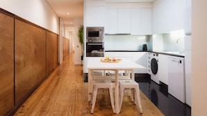 Une cuisine moderne avec des meubles blancs, un plancher en bois et un coin repas comprenant une table et des chaises.