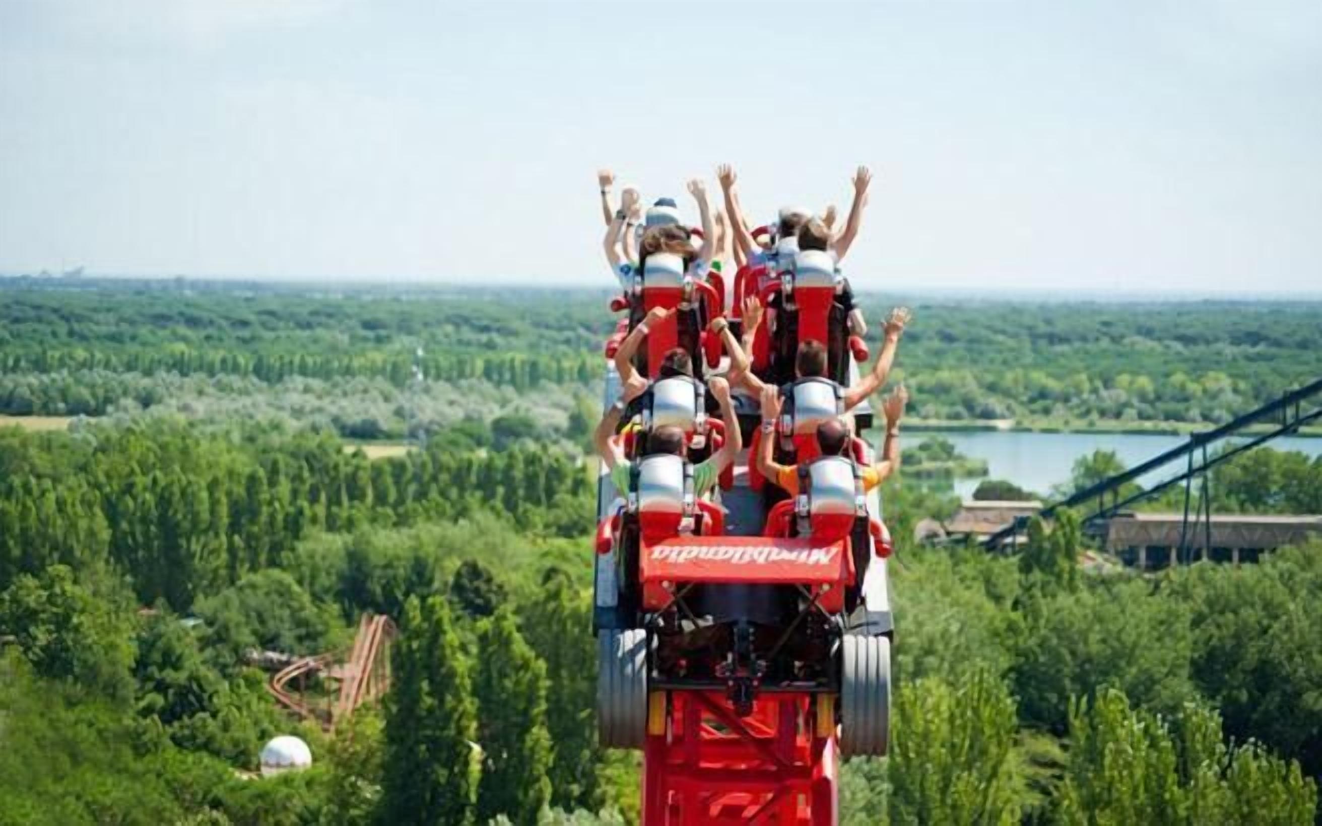 Een groep mensen op een rode achtbaan met een mooi uitzicht op een bos en een meer.