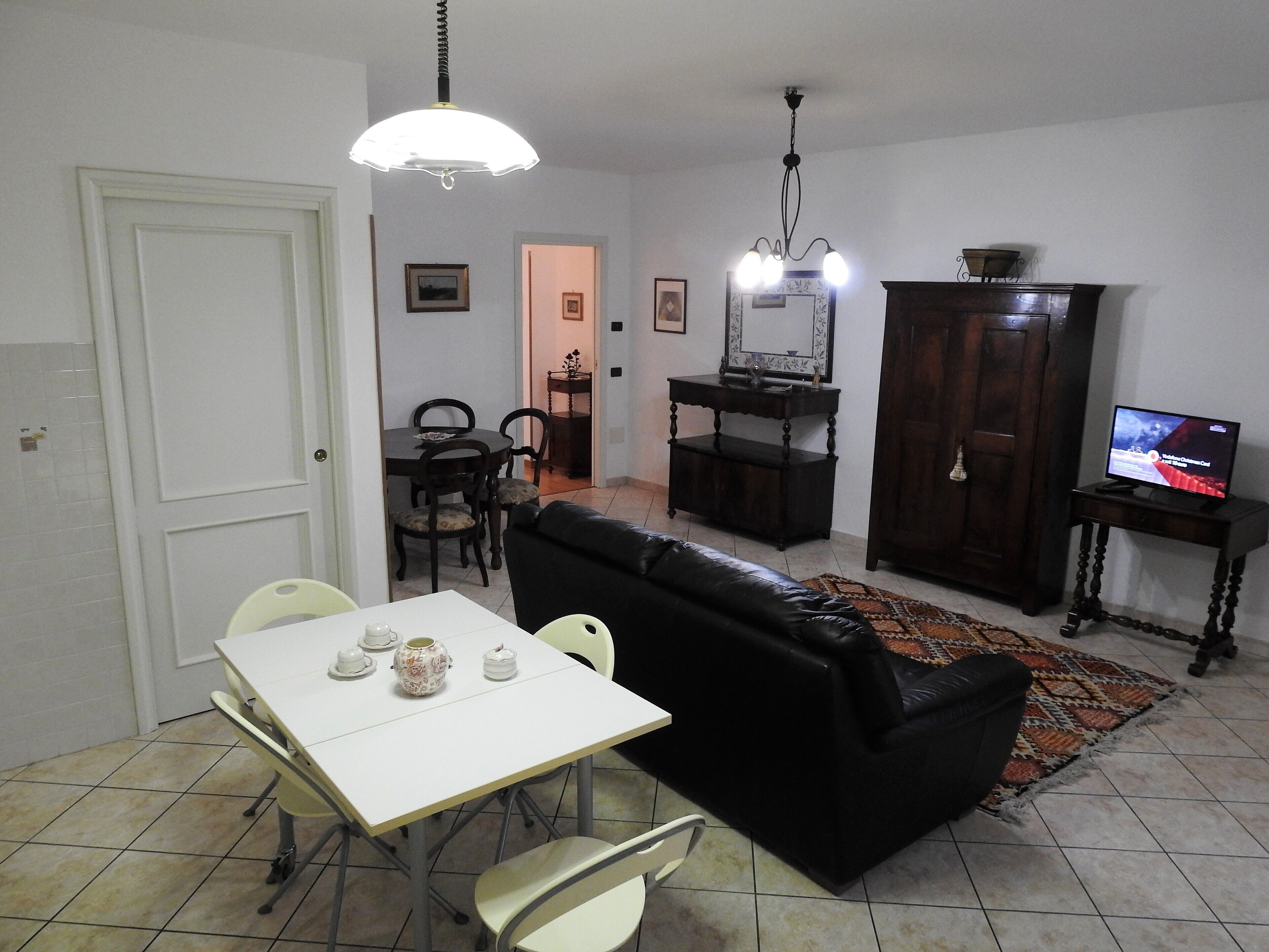 A living room with a white table, black sofa, and a TV on a stand.