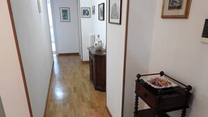 Un couloir doté d’un plancher en bois, une petite table en bois foncé sur laquelle se trouve une assiette de nourriture, et un radiateur.