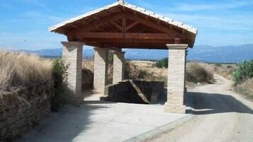 A stone pavilion with a tiled roof, situated on a dirt path with mountains in the background.