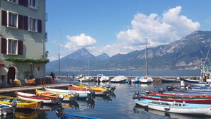 A marina with colorful boats docked, a building with outdoor seating, and mountains in the background. - Villa on LAKE with private dock.  (BRENZONE SUL GARDA)