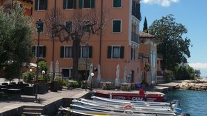 A row of colorful boats docked at a waterfront, with a building featuring balconies and outdoor seating in the background. - Villa on LAKE with private dock.  (BRENZONE SUL GARDA)