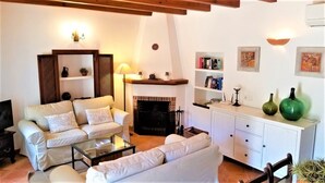 A living room with a fireplace, white sofas, a coffee table, and a bookshelf. - Beatiful and peaceful villa with amazing views into the mountains  (Sóller)