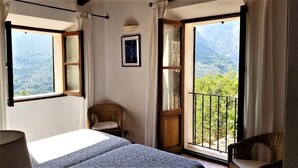 A bedroom with a large window, a bed, a chair, and a view of a mountainous landscape. - Beatiful and peaceful villa with amazing views into the mountains  (Sóller)