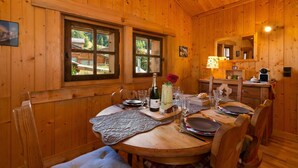 Un interior de madera con una mesa de comedor preparada para cuatro personas, una botella de champán y un jarrón con flores rojas.