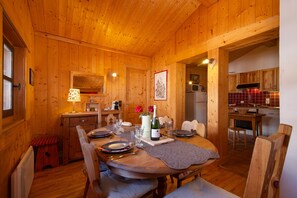 A wooden cabin interior with a dining area, kitchen, and a cozy living space.