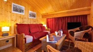 Un acogedor interior de cabaña de madera con sofá, sillas, una mesa y un televisor.