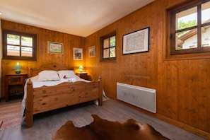 A wooden-paneled room with a bed, framed pictures, a radiator, and a cowhide rug.