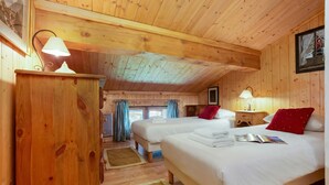 Una habitación tipo cabaña de madera con dos camas, un aparador de madera y una ventana con cortinas.