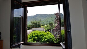 A room with a large window, curtains, and a view of a mountain and greenery. - Spacious Villa with large private Pool and Air-conditioning in all 5 bedrooms (Les Aires)