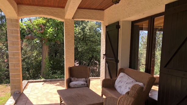 A covered patio area with wicker furniture, including a sofa and a table, and a view of the surrounding greenery. - Spacious Villa with large private Pool and Air-conditioning in all 5 bedrooms (Les Aires)