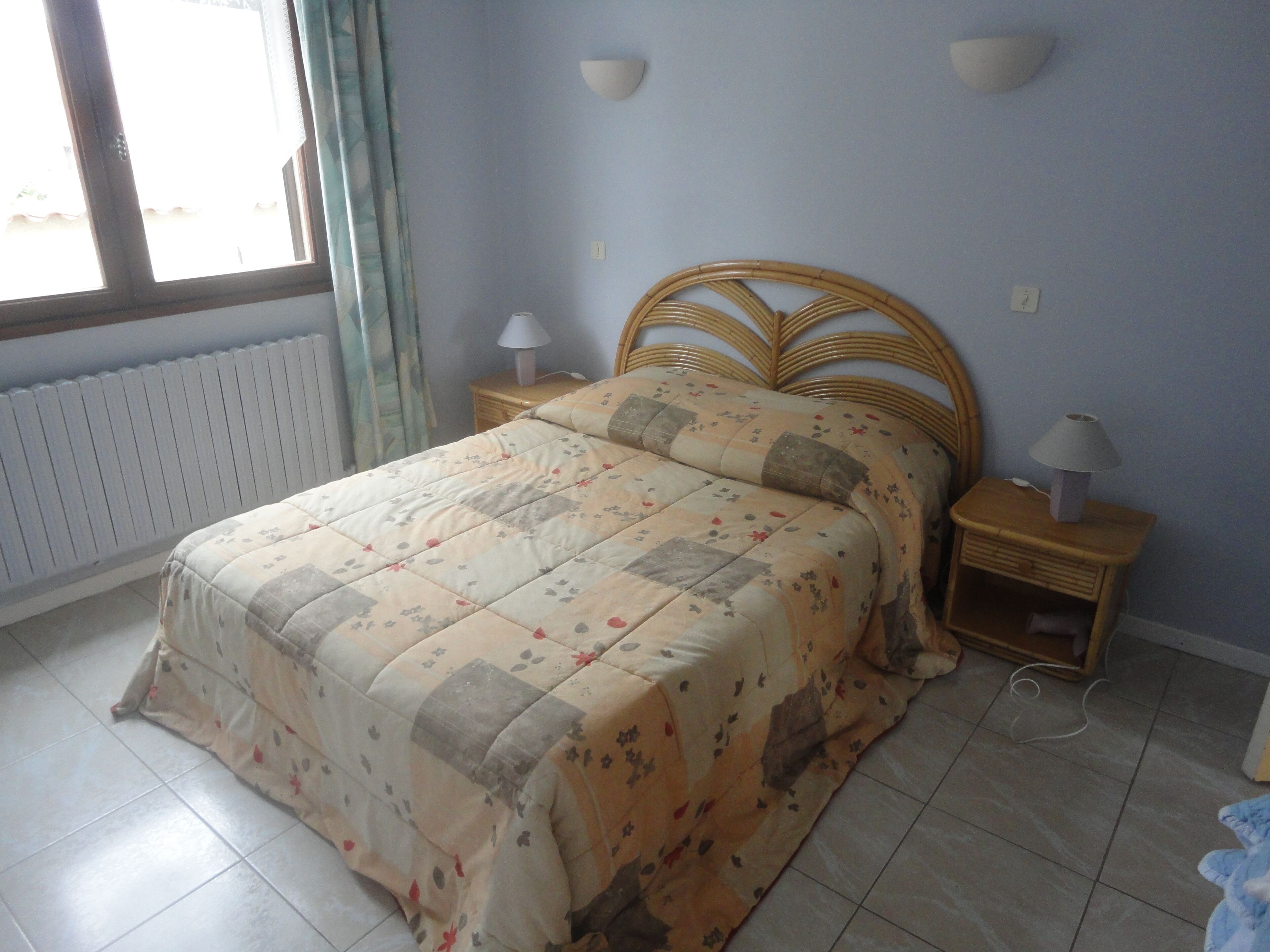 Une chambre à coucher avec un lit, deux tables de chevet avec des lampes, une fenêtre avec des rideaux et un radiateur.