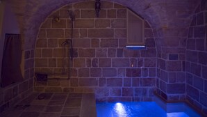 Ein Badezimmer mit Steinwänden, einer eingebauten Badewanne, einer Dusche und einer Wandleuchte.