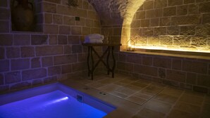 Ein Zimmer mit Steinwänden, einer Badewanne, einem kleinen Tisch mit einem Handtuch und einem Wandregal.