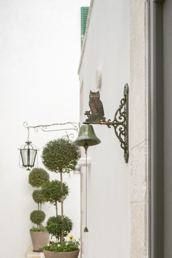 A wall-mounted bell and owl decoration, a hanging lantern, and potted plants.
