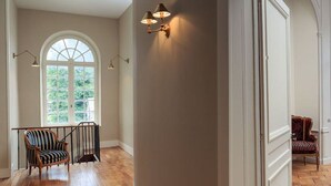 A spacious room with a large arched window, a wooden floor, and two upholstered chairs.