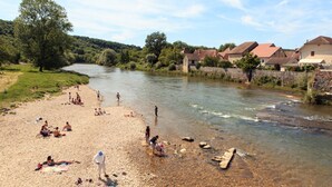 A riverside beach with people sunbathing and swimming, surrounded by houses and greenery.