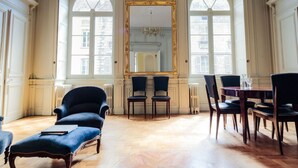 A spacious room with a large mirror, two armchairs, a dining table with chairs, and a fireplace.