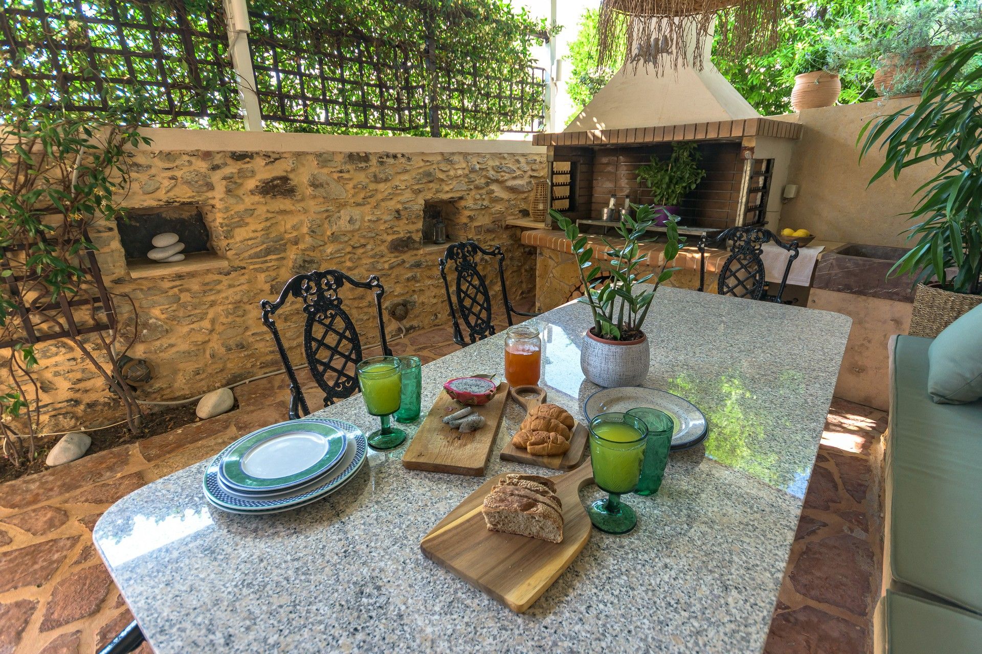 Un espace extérieur aménagé pour les repas, avec un mur en pierre, un barbecue et une variété de plats et de boissons disposés sur la table.