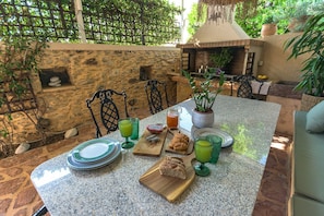 Un'area pranzo all'aperto con un muro in pietra, un barbecue e diversi cibi e bevande sul tavolo.