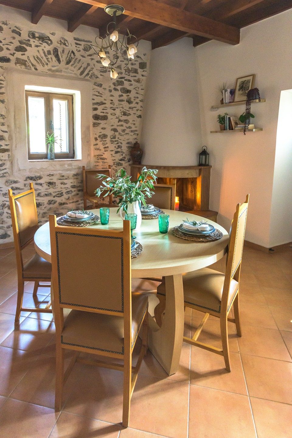Un coin repas avec une table ronde, quatre chaises, un vase avec des plantes vertes et une cheminée en arrière-plan.