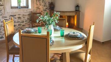 Un coin repas avec une table ronde, quatre chaises, un vase avec des plantes vertes et une cheminée en arrière-plan.