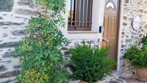 Edifici de pedra amb porta i finestra de fusta, plantes en testos i sòl de pedra.
