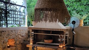 Zona d'esmorzar a l'aire lliure amb una paret de pedra, una làmpada penjant de fibra natural i un forn de rajola.