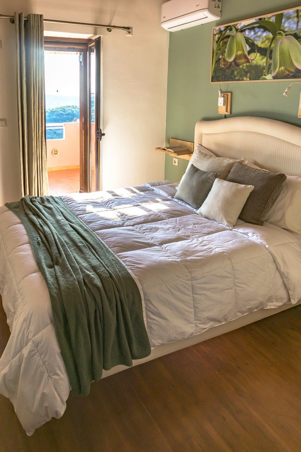 Une chambre à coucher avec un lit, une table de chevet, une fenêtre avec des rideaux et une vue sur l’extérieur.