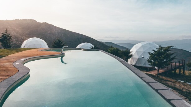 Una piscina con muelle de madera, rodeada de estructuras blancas en forma de cúpula, con montañas al fondo.