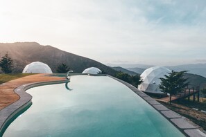 Una piscina con muelle de madera, rodeada de estructuras blancas en forma de cúpula, con montañas al fondo.
