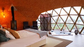 Un dormitorio acogedor con cama, bañera de hidromasaje y un amplio ventanal con vistas al exterior.