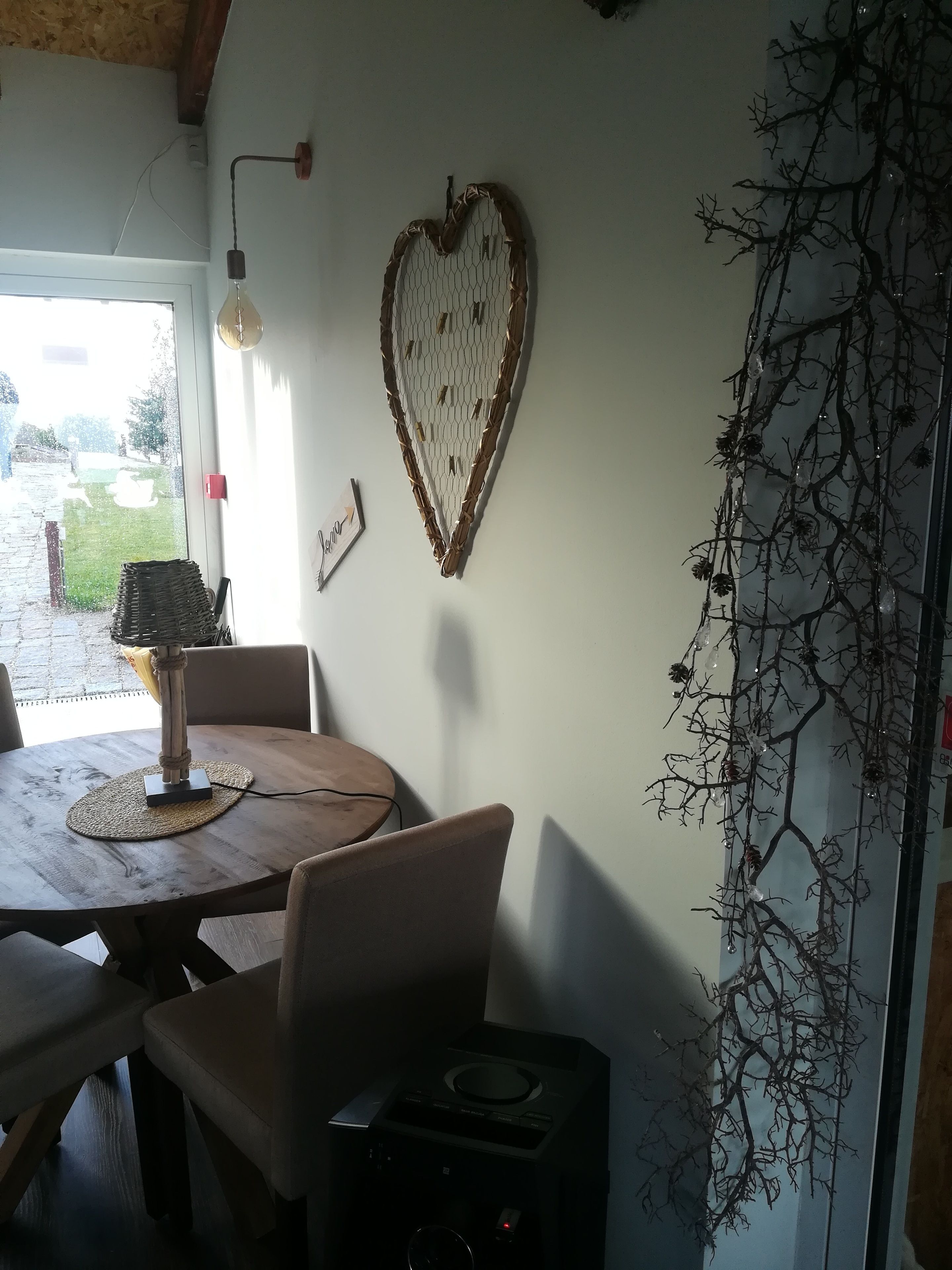 Un comedor con una mesa redonda de madera, sillas, una lámpara y una decoración en forma de corazón en la pared.