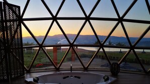 Una bañera de hidromasaje en una habitación con un ventanal que da a un paisaje con montañas y una masa de agua.
