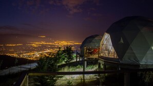Una estructura en forma de cúpula con una plataforma de cristal para observar una vista nocturna de la ciudad.