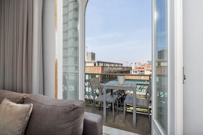 A balcony with a view of a building and construction cranes, a table with chairs, and a sofa with cushions.
