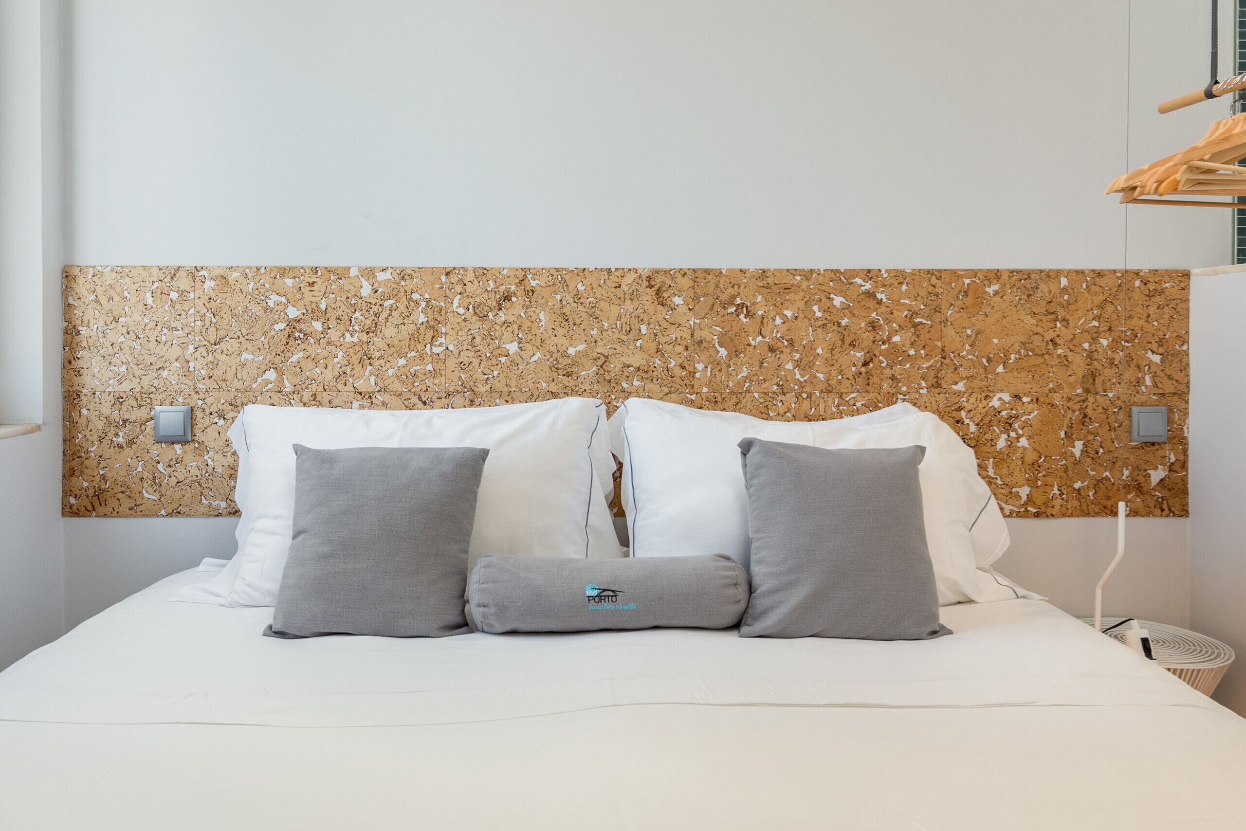 A bed with a cork headboard, white bedding, and two gray pillows.