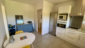 Eine moderne Küche mit Essbereich, ausgestattet mit Kühlschrank, Mikrowelle, Backofen und einem kleinen Tisch mit Stühlen.