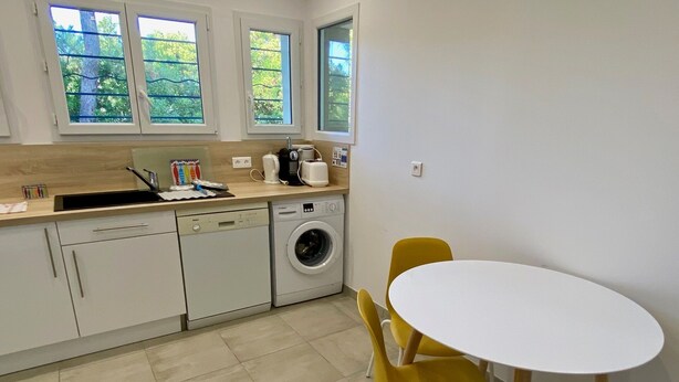 A compact kitchen with a washing machine, a sink, and a small dining area with two yellow chairs. - Ideal beach location close to the Pointe in Cap Ferret with lovely terrace (Lège-Cap-Ferret)