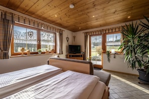 Ein Zimmer mit zwei Betten, einem Fernseher und großen Fenstern mit Vorhängen.