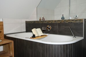 Un baño moderno con una bañera independiente, un estante de madera y un espejo sobre la bañera.