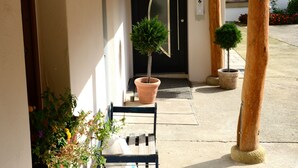 Un espacio al aire libre cubierto con un banco de madera, plantas en macetas y una puerta que da a un edificio.