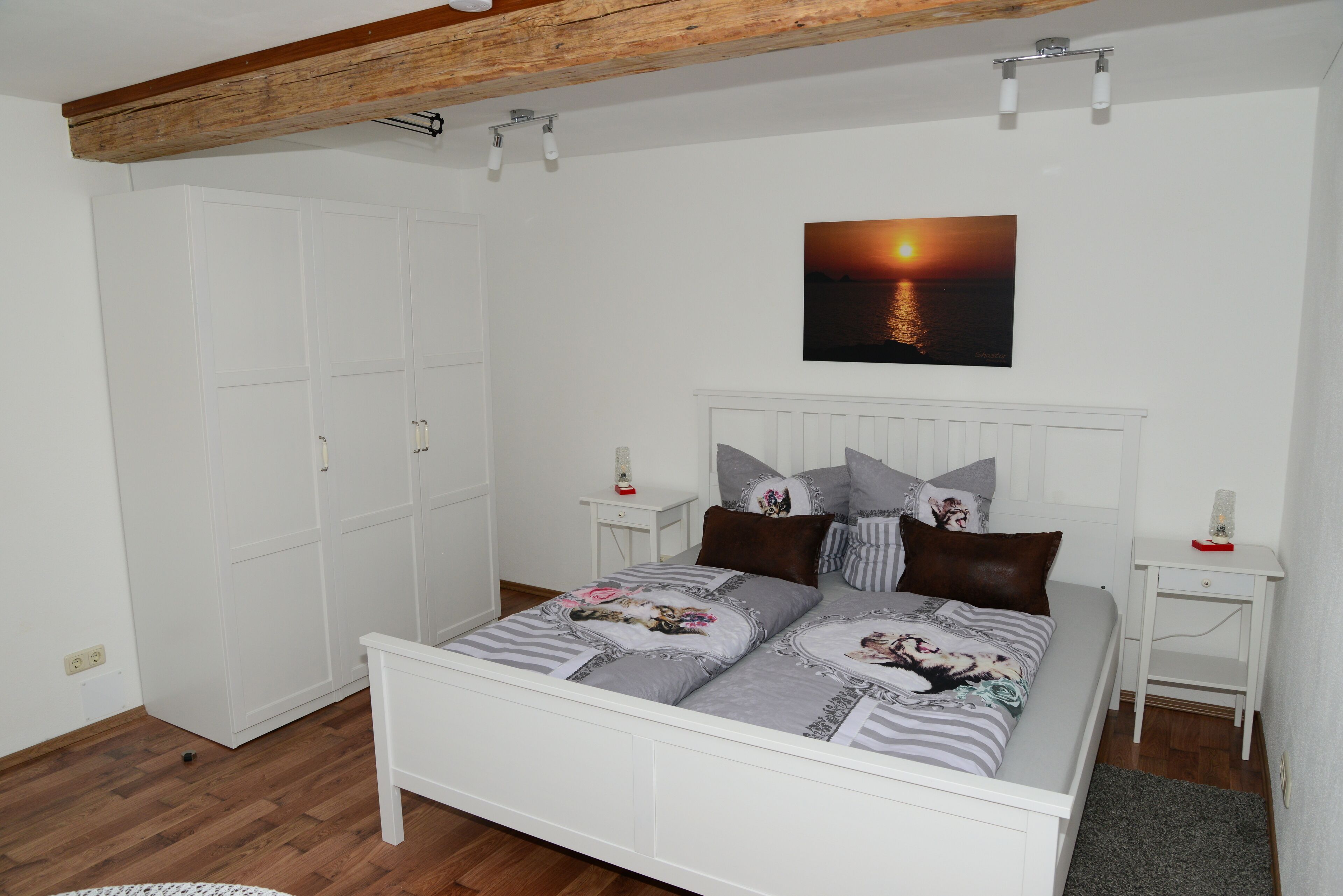 Un dormitorio con cama, armario blanco y un cuadro de un atardecer.