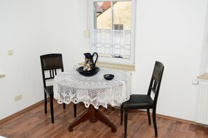 Un pequeño comedor con un mantel de encaje blanco, dos sillas negras, una jarra negra y un bol en la mesa.