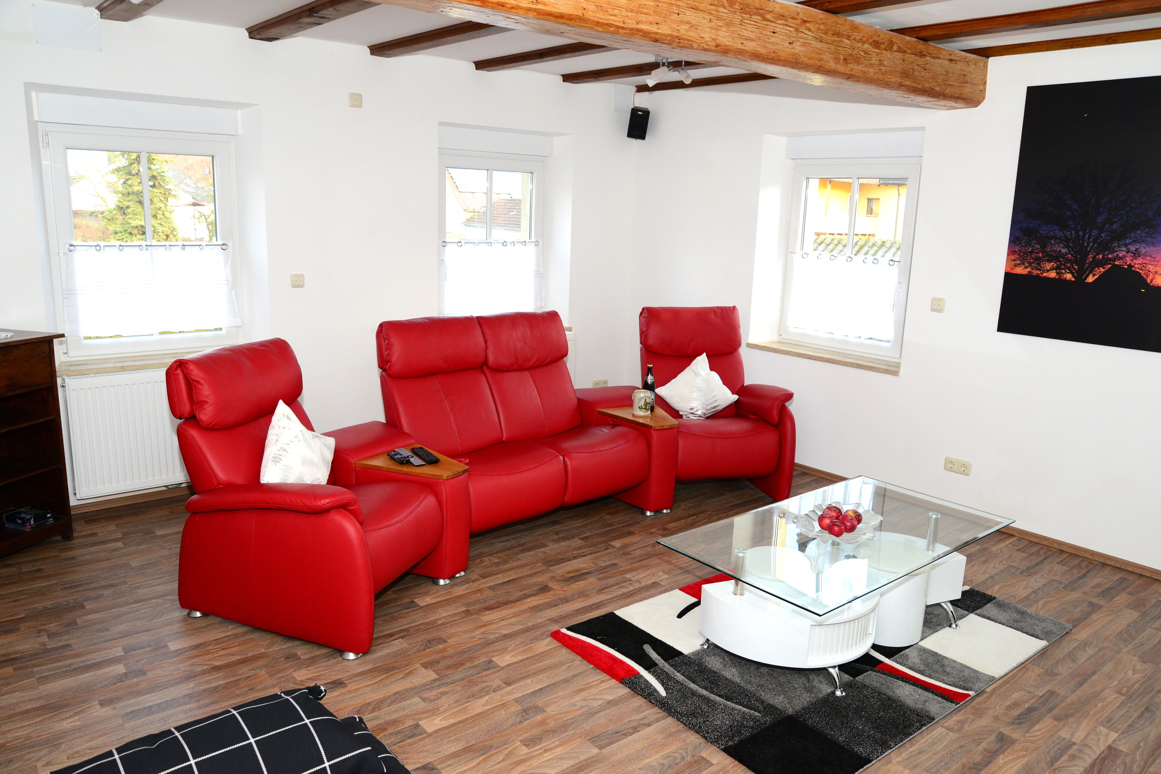 A modern living room with a red leather sofa, a glass coffee table, and a black and white rug.